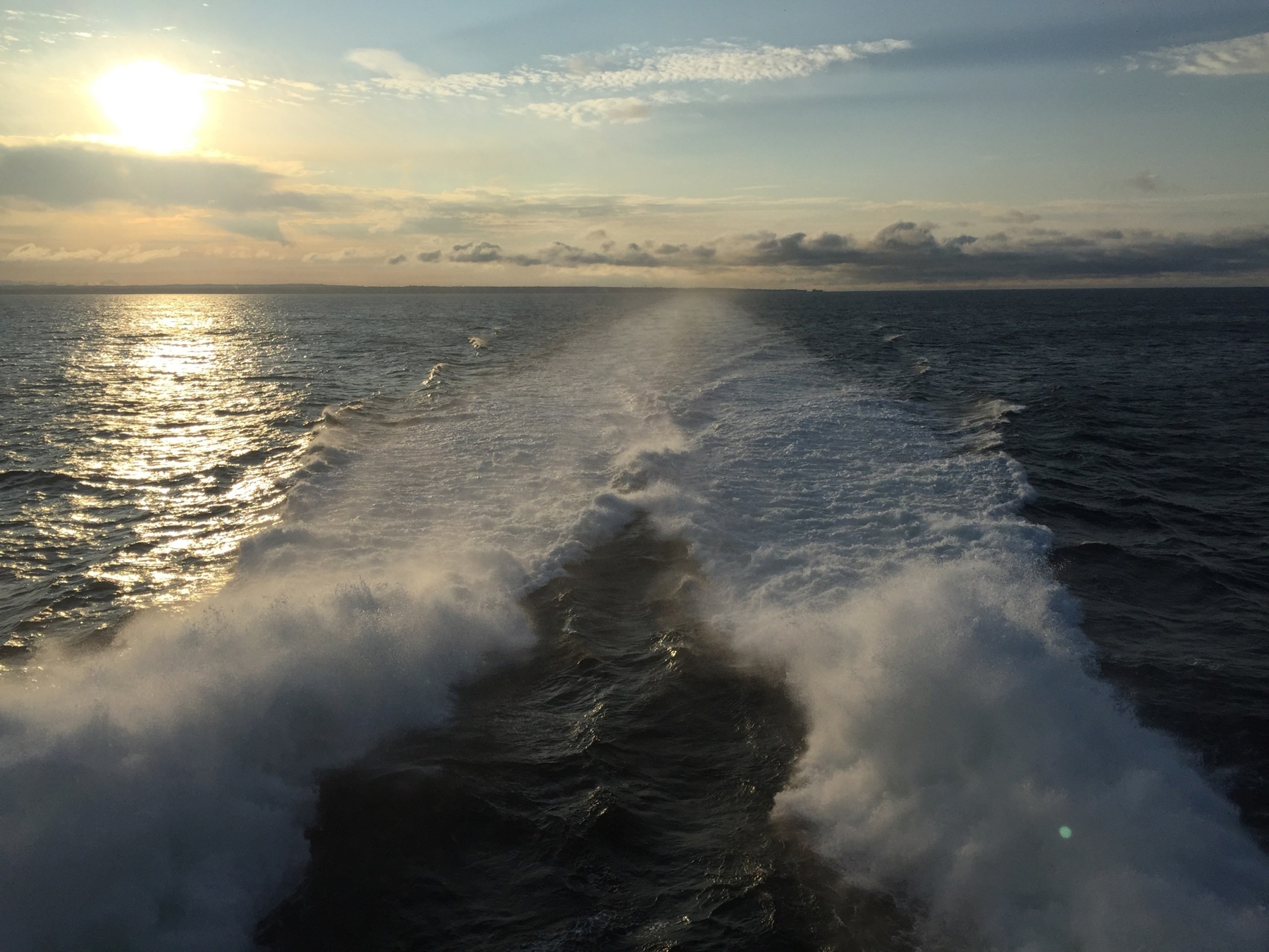 Bølger bag en færge i solnedgangen.