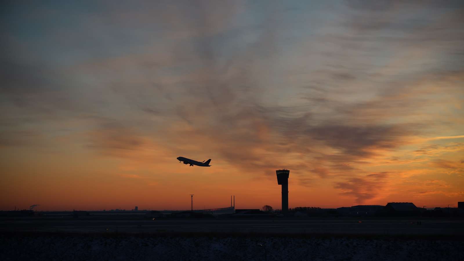 Solopgangshimmel, hvor man kan se silhuetten af et fly og Tårnet i Københavns Lufthavn