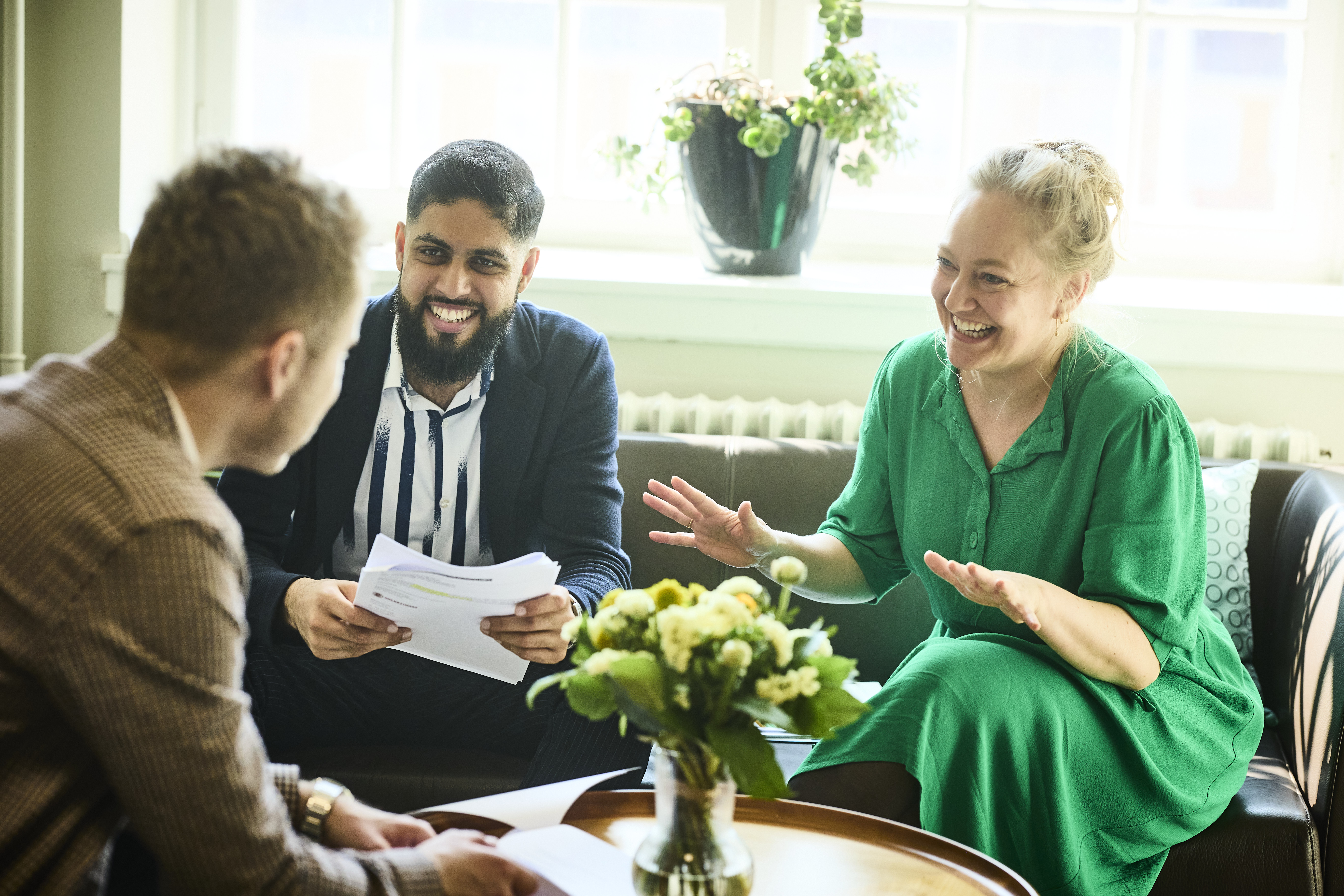 Tre ansatte i departementet har en samtale i en sofa