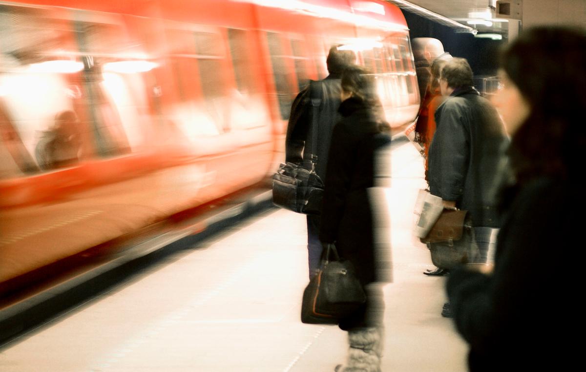 Rødt S-tog ses holde ved perron, imens passagerer venter på at stige ombord.