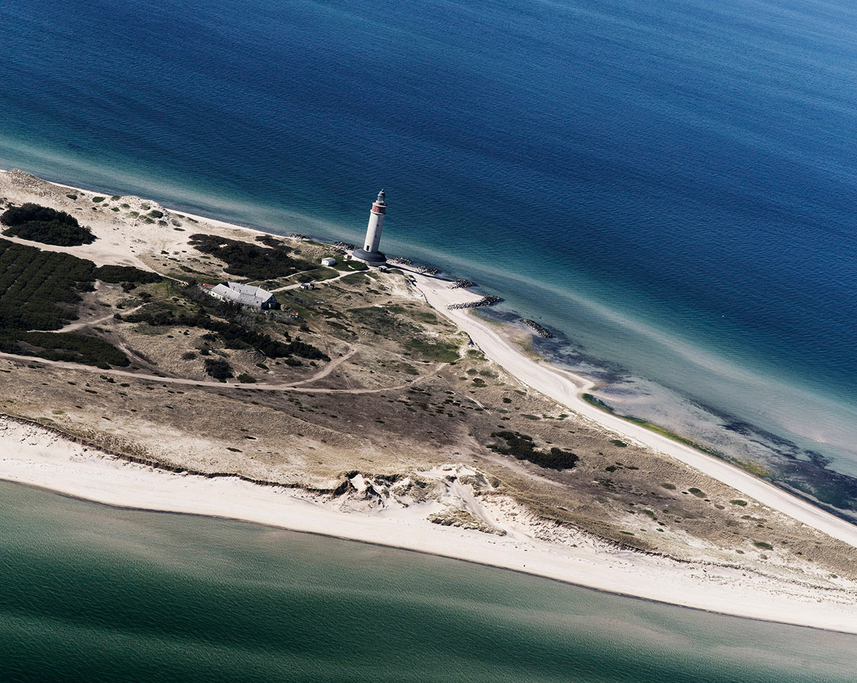 Luftfoto af landtange med fyrtårn og vand på tre sider.