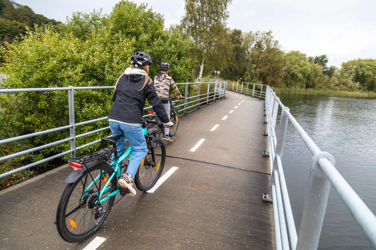 To skolebørn cykler sammen over en lille bro